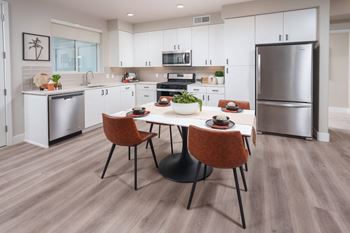 Interior of a model apartment showing kitchen with stainless steel appliances that include a dishwasher, fridge/freezer, microwave and gas range